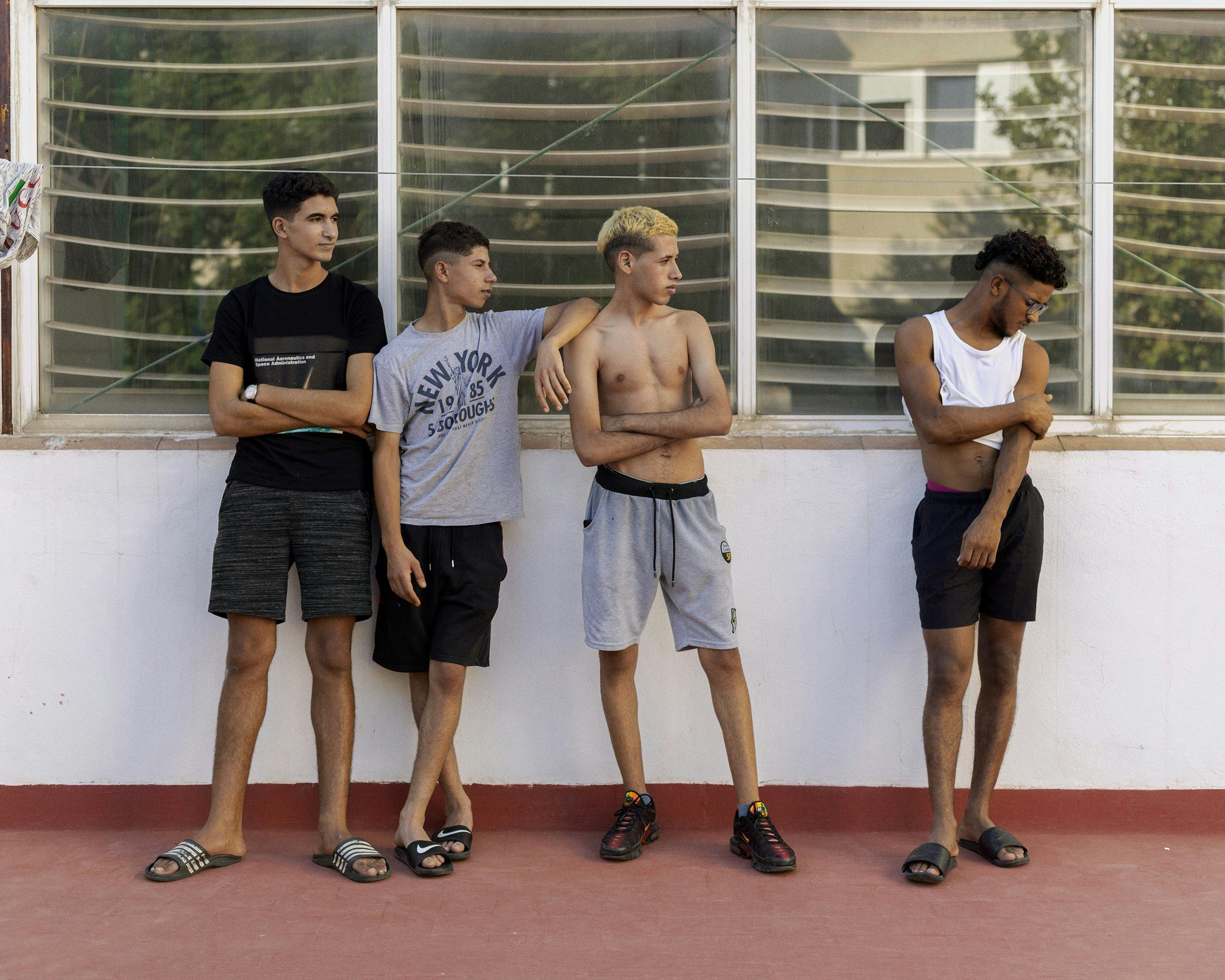 Image of four young men standing in a row in front of a window. © Felipe Romero Beltrán